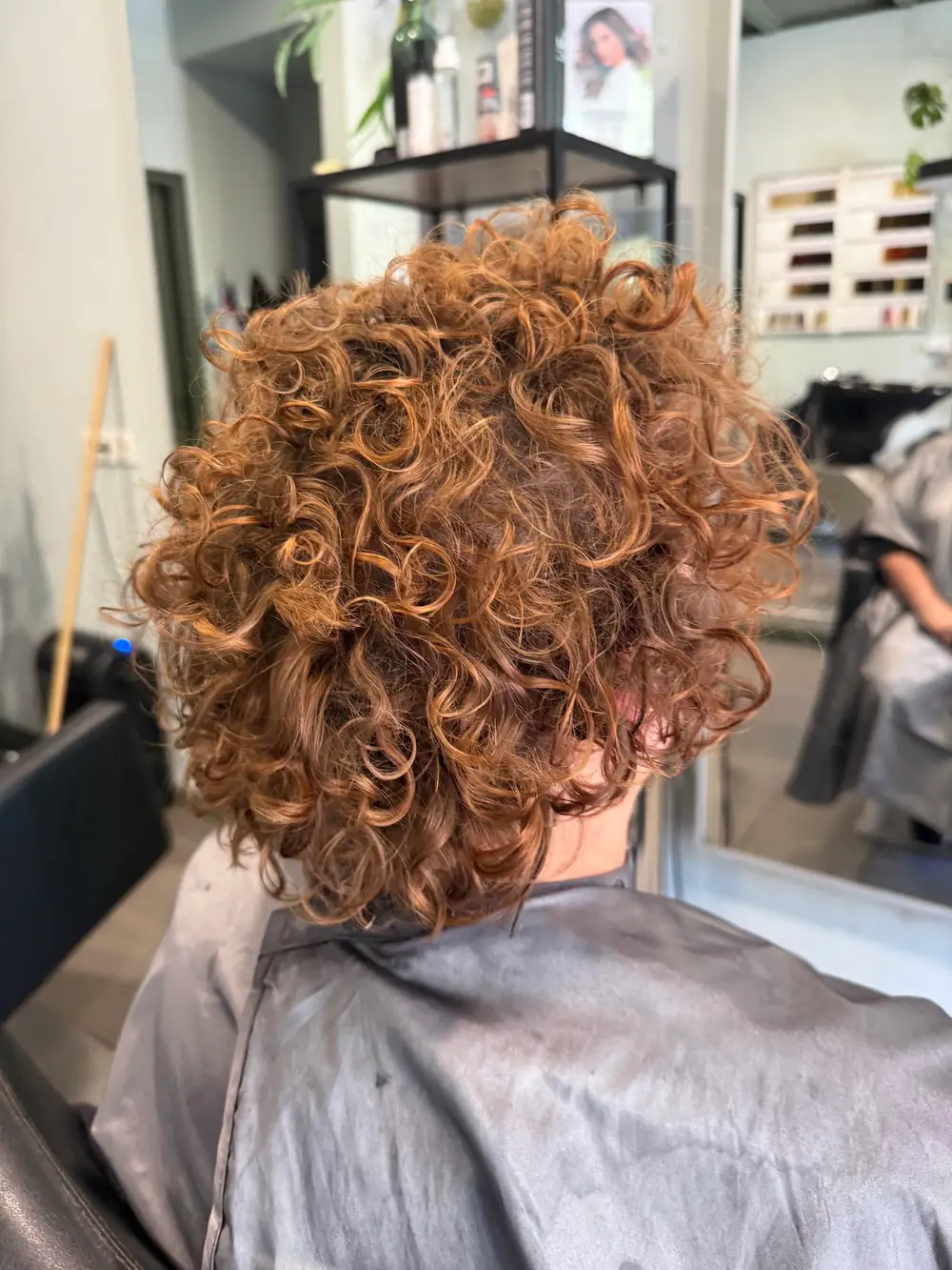 Achterkant van een kort koperkleurig krullenkapsel, net geknipt in de salon